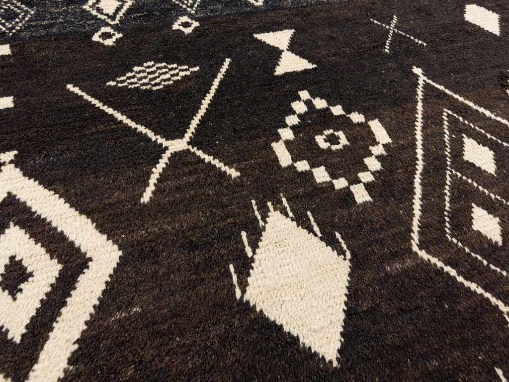 Dark brown tribal rug hand knotted of wool with warm ivory accent colors.
